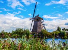 Molino de viento al lado de un canal rodeado de vegetación y con un cielo azul