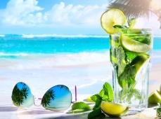 foto de unas gafas de sol junto a un vaso de bebida tropical en la arena de la playa