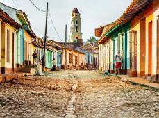 Calle empedrada de estilo colonial con casas a los lados de colores, al final se ve el campanario de una iglesia
