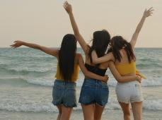 tres niñas de espaldas abrazadas mirando al mar