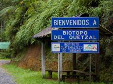 Letrero en azul dando la bienvenida delante de una caseta de madera y rodeado de vegetación
