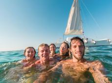 Grupo de personas en el mar haciéndose un selfi delante de un velero