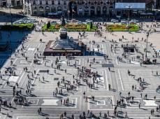 Plaza con una estatua en el centro y llena de gente paseando