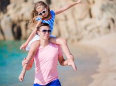 Un hombre con una niña en sus hombros por la playa