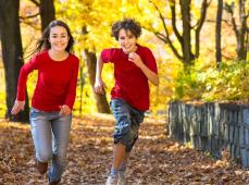 dos niños con jersey rojo corriendo por un sendero lleno de hojas