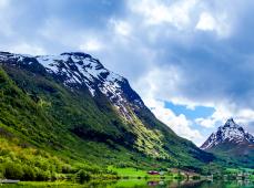 Montañas verdes con nieve y un cielo con nubes