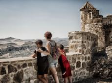 Una mujer y dos niños de espaldas apoyados en una muralla mirando el paisaje