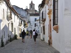 Calle empedrada con las casas en color blanco y con gente de espalda paseando