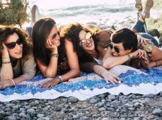 Tres chicas y un chico tumbados en una toalla soriendo