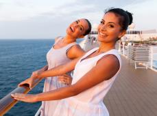 Dos chicas sonriendo vestidas de blanco agarradas en una cubierta del barco