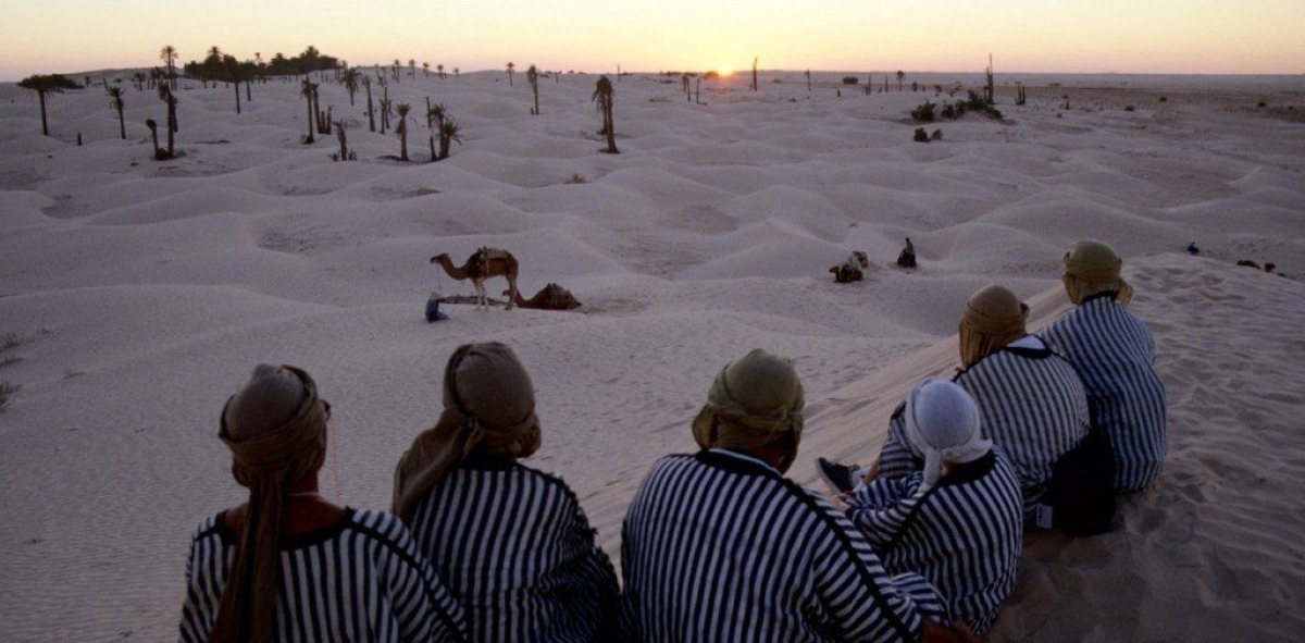 Grupo de solteros viajeros de espaldas vestidos con túnicas admirando el atardecer en el desierto