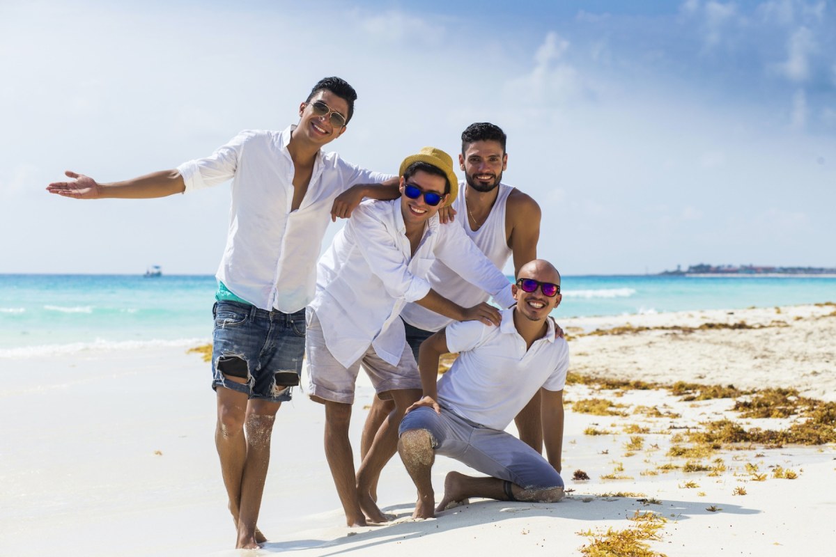 Cuatro chicos de blanco posando en la playa, al fondo el mar