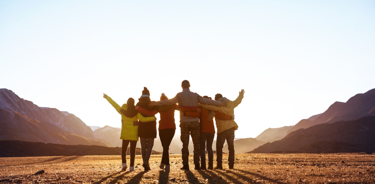 Grupo de chicos y chicas abrazados disfrutando del atardecer en la montaña