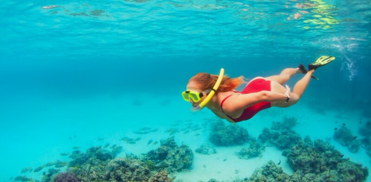 Mujer con bañados rojo haciendo esnórquel en la playa
