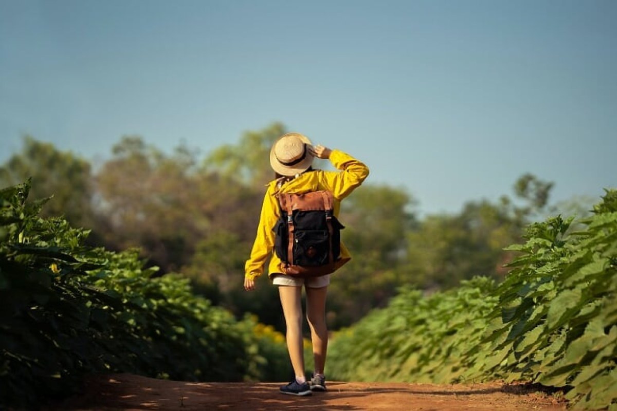 Chica de espaldas con pantalón corto y sombrero siguiendo un camino de tierra rodeado de vegetación