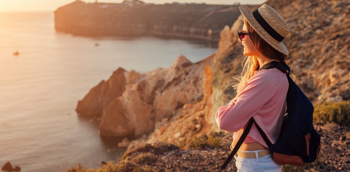 Soltera viajera contemplando al atardecer el mar desde unos acantilados