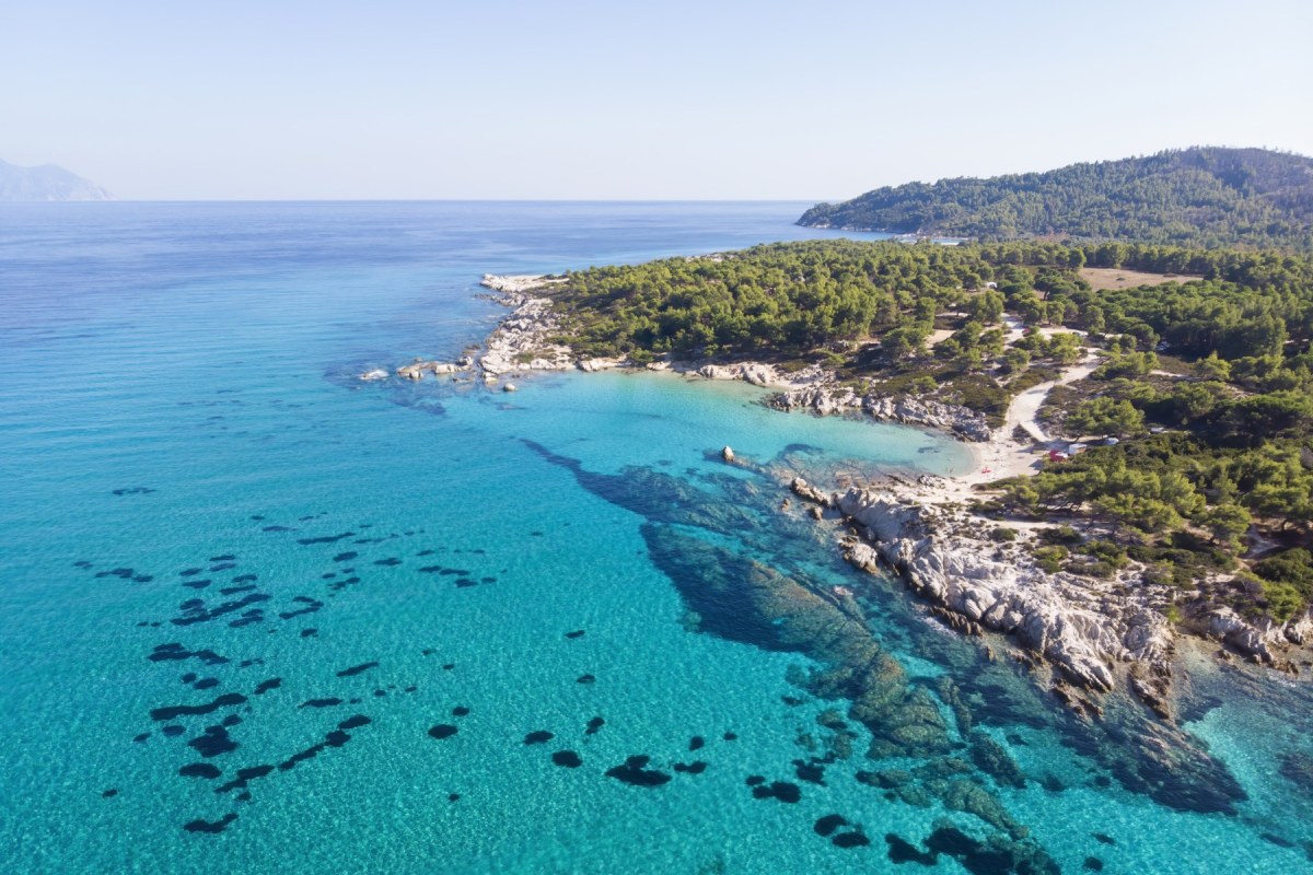 Costa rocosa del mar Egeo en Grecia, con aguas turquesas cristalinas que gradúan del azul profundo al verde claro cerca de la orilla.
