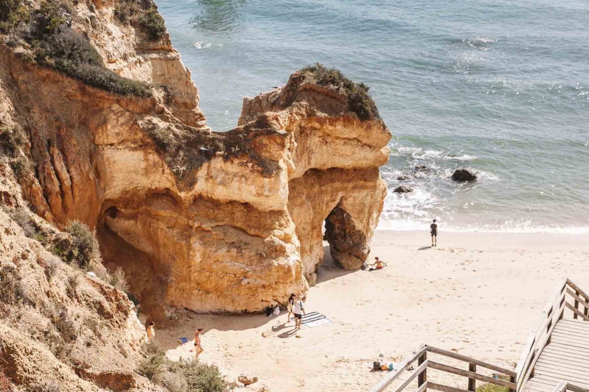 dos niñas bajando por una escalera de madera a la playa que esta rodeada de rocas entrando al mar