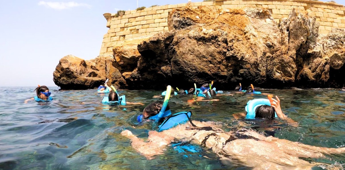 grupo de jóvenes haciendo snorkel al lado de unas piedras en el mar
