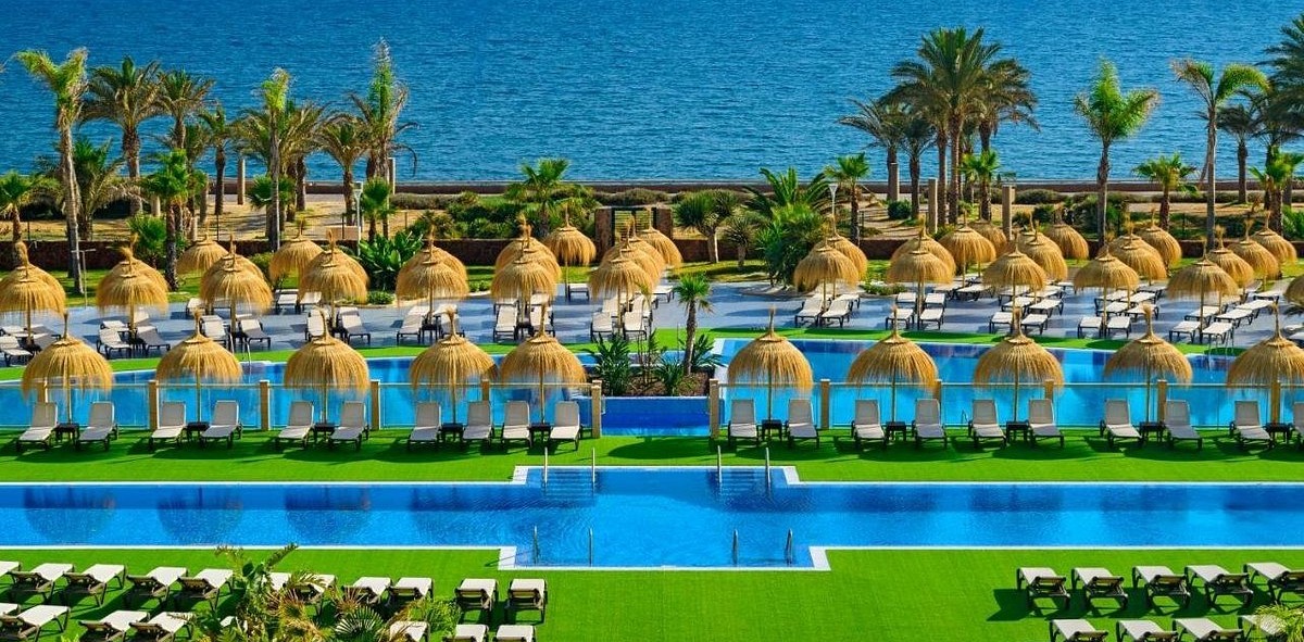 Piscina con hamacas y sombrillas de paja mirando al mar