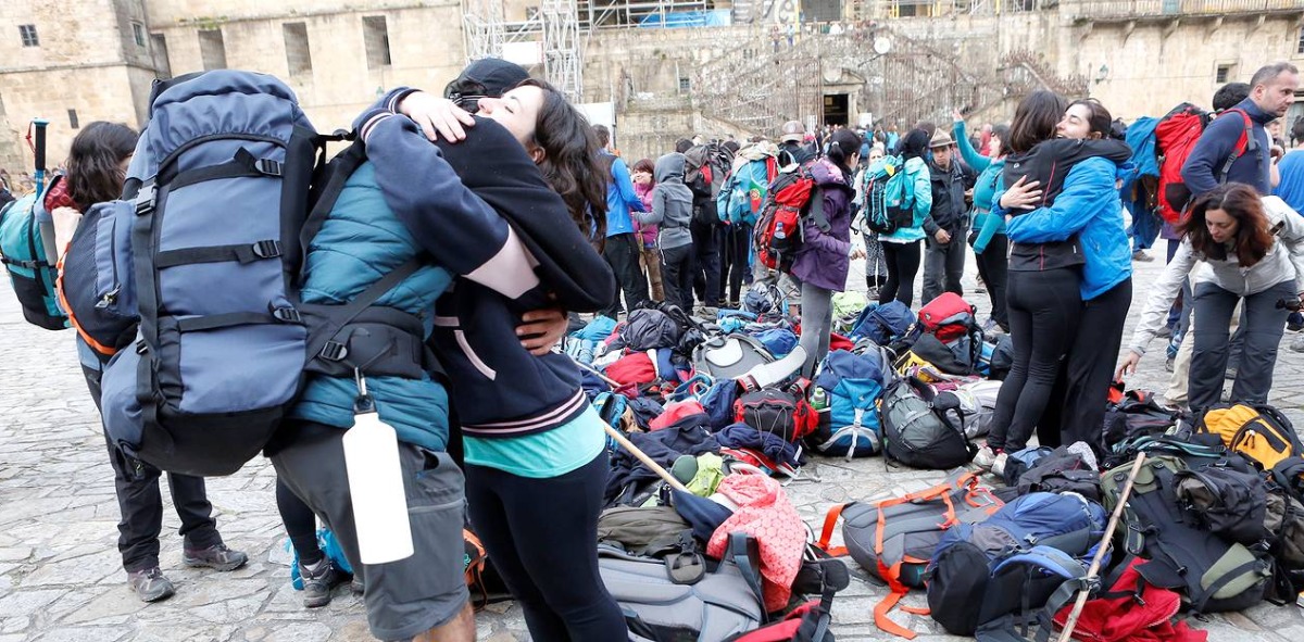 Grupo abranzandose con todas las mochilas en la plaza, al fondo las escalinatas para subir a la catedra