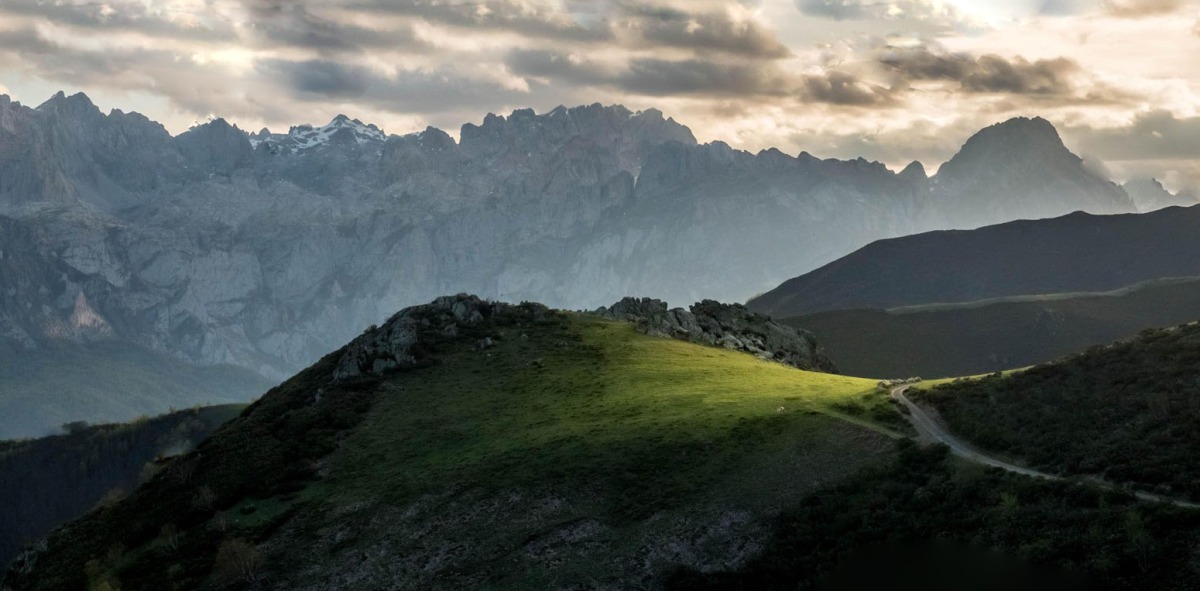 Al fondo montañas escarpadas y delante una carretera con montañas verdes