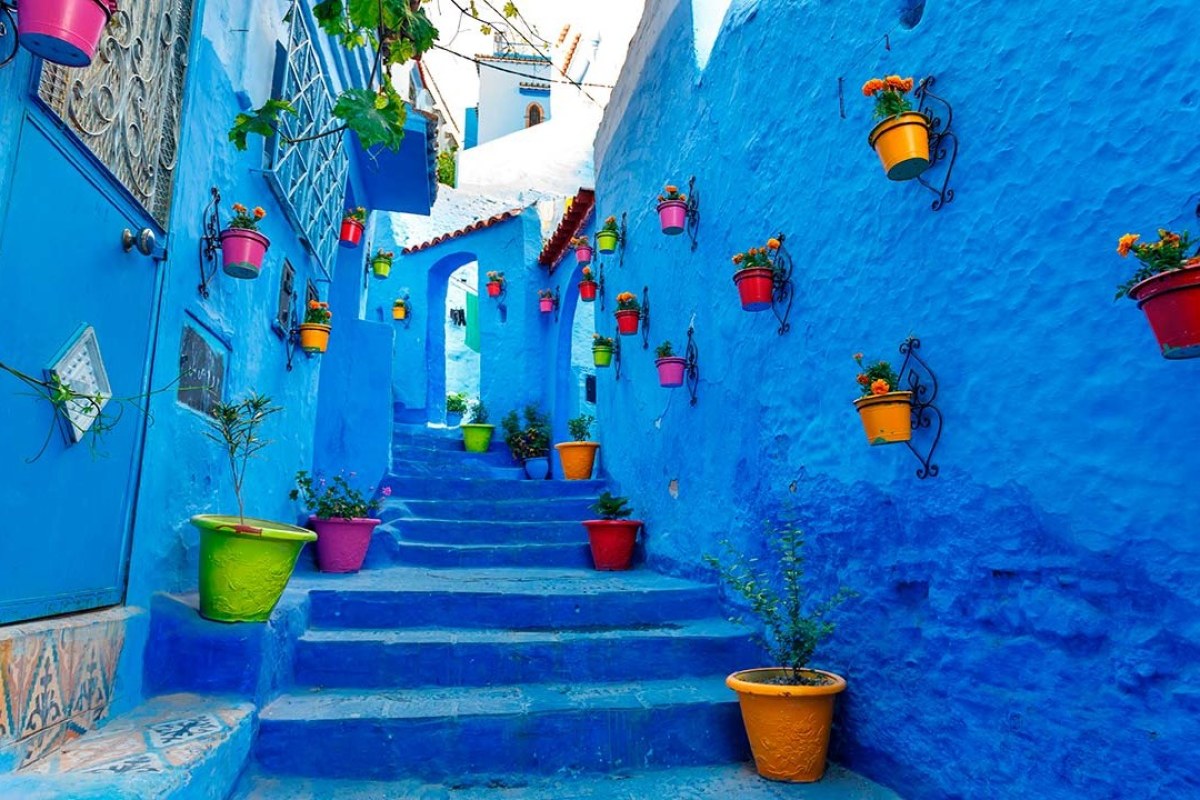 Calle de color azul con escaleras y las paredes decoradas con tiestos llenos de flores
