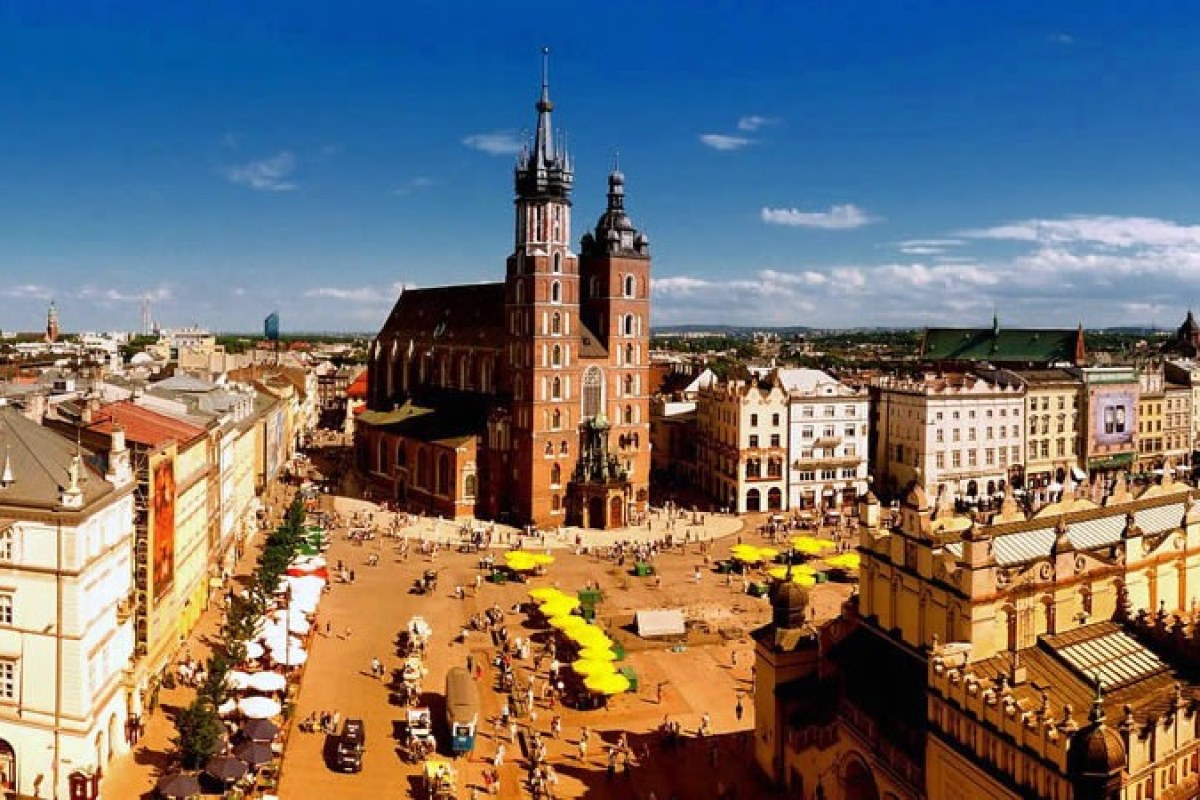 Panorámica de una plaza con una iglesia de dos torres y en la plaza muchas terrazas con sombrillas