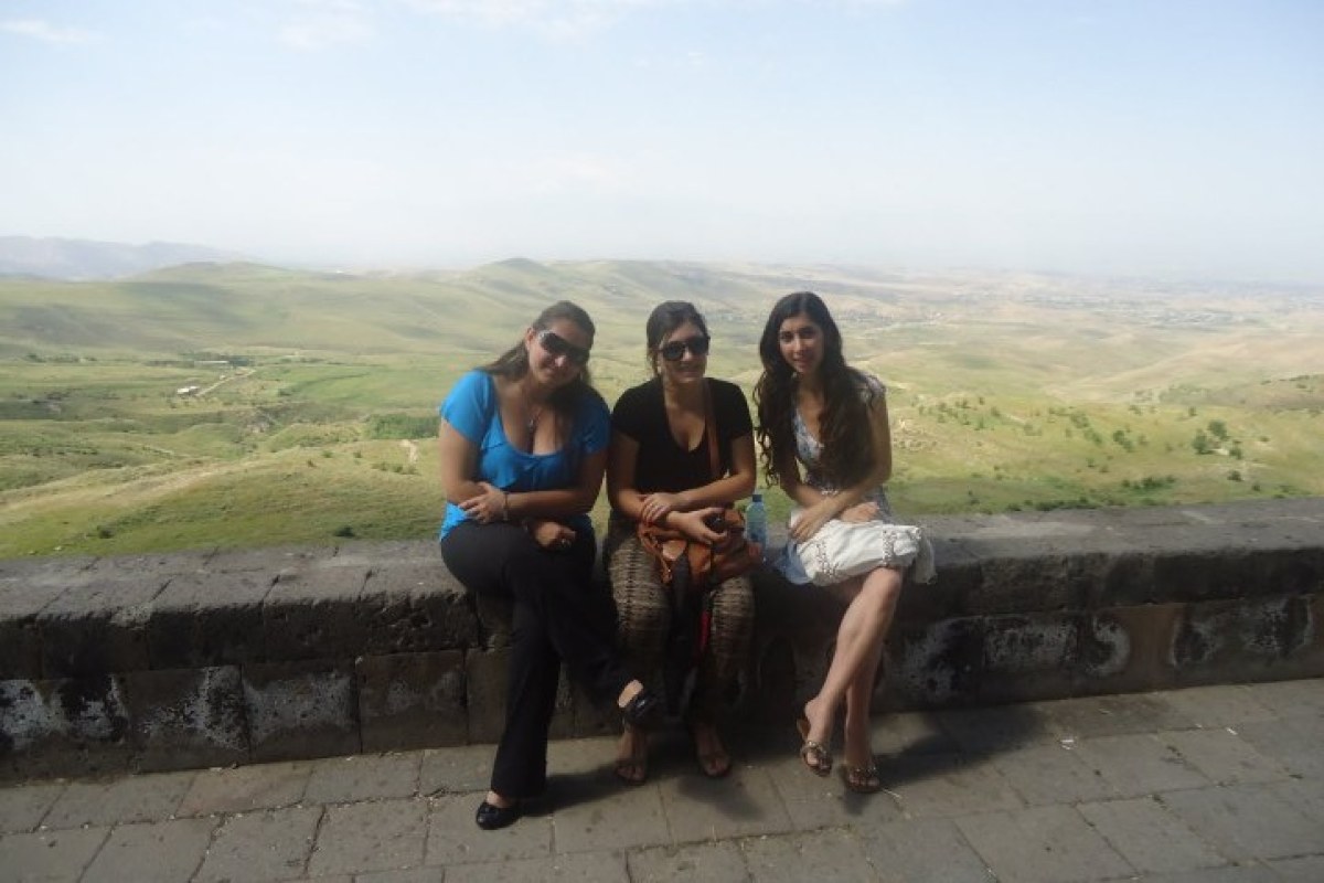 Tres chicas sentadas en una valla de piedra y de fondo un valle verde