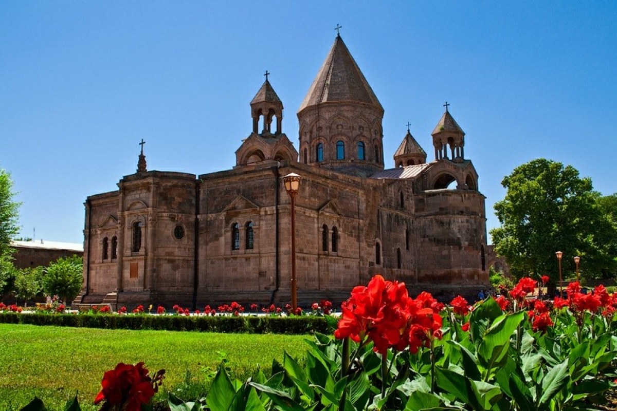 Catedral antigua de color marrón oscuro en medio de un parque lleno de flores rojas