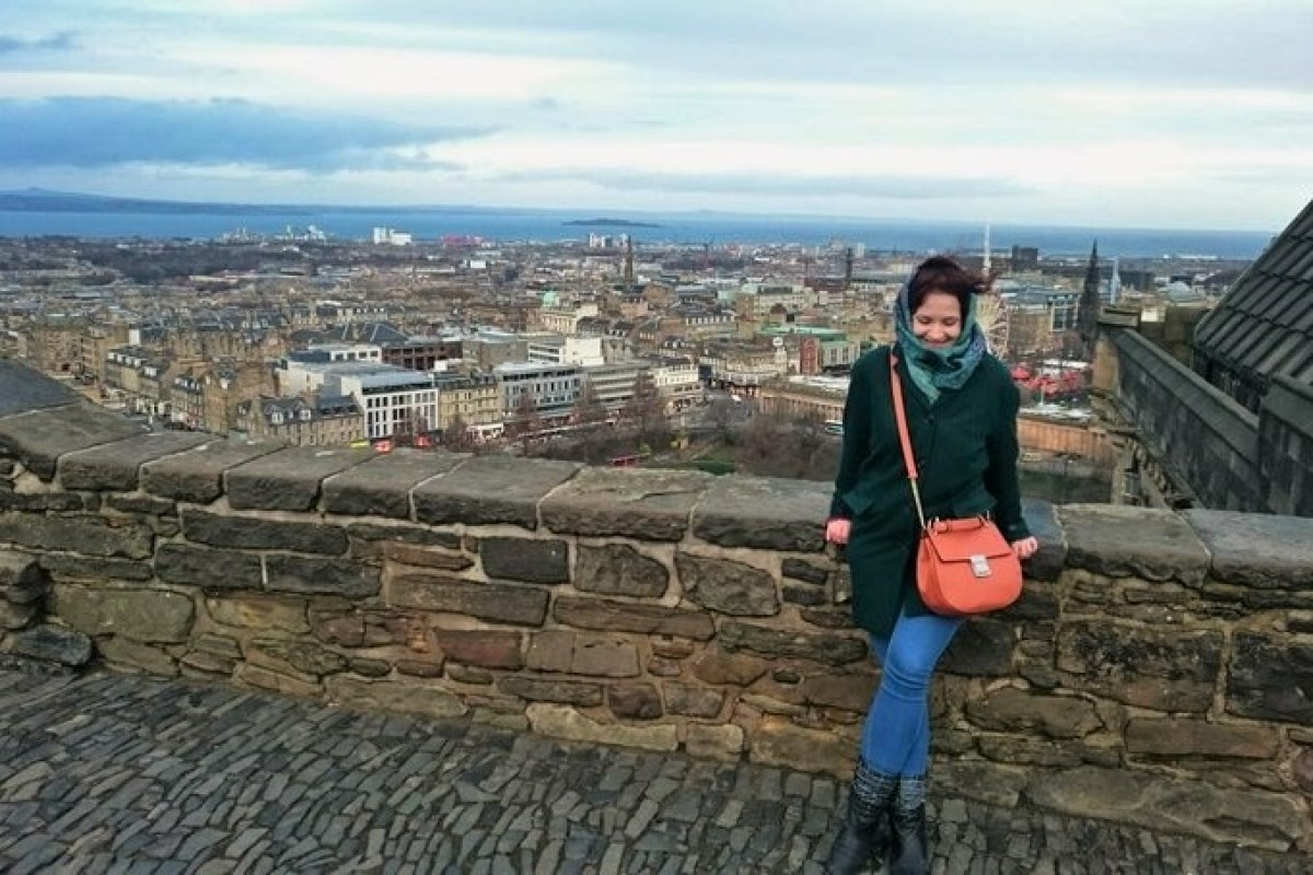 Soltera Viajera apoyada en una muralla de piedra y al fondo una panorámica de la ciudad