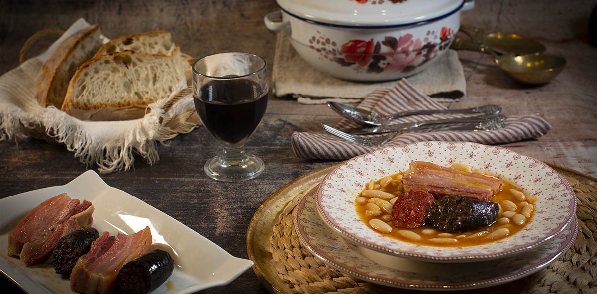 Un plato de fabada en una mesa con una copa de vino