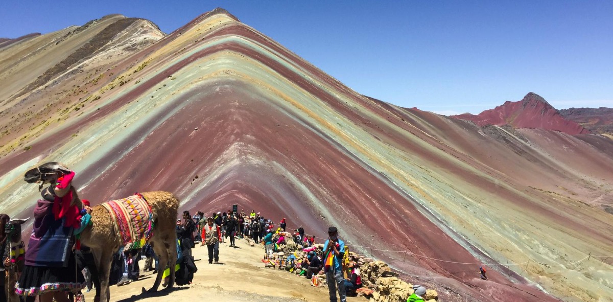 Montaña de colores al fondo rodeada de mucha gente y asnos