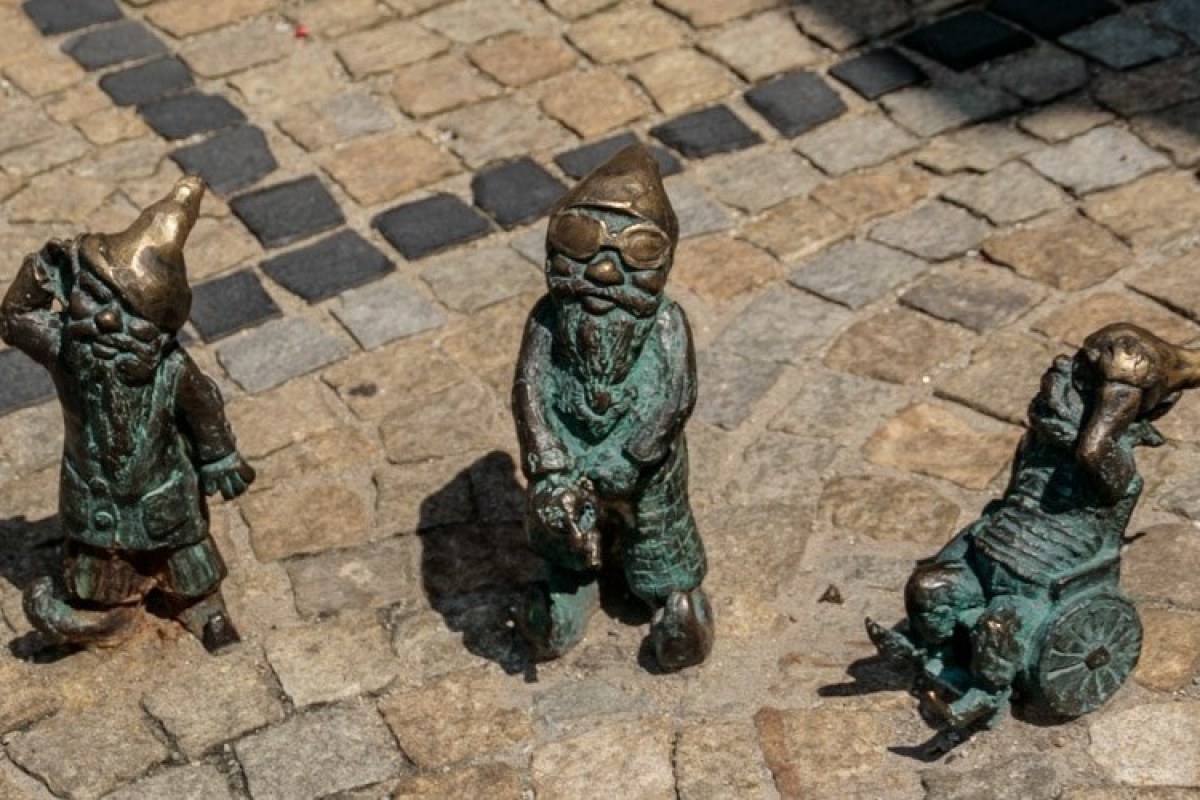 Tres estatuas de bronce de tres enanitos en un suelo empedrado