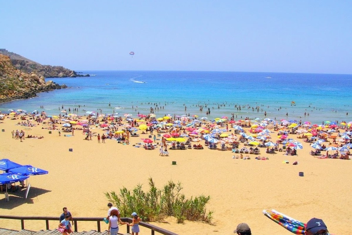 Panoramica de una playa de arena blanca con muchas sombrillas, gente bajando por una escalera de madera a la playa