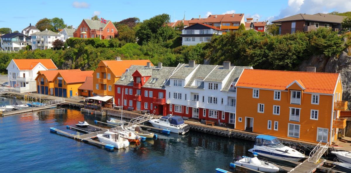 Casas de madera en colores rojos y naranjas a las orillas de un fiordo con barcas de recreo