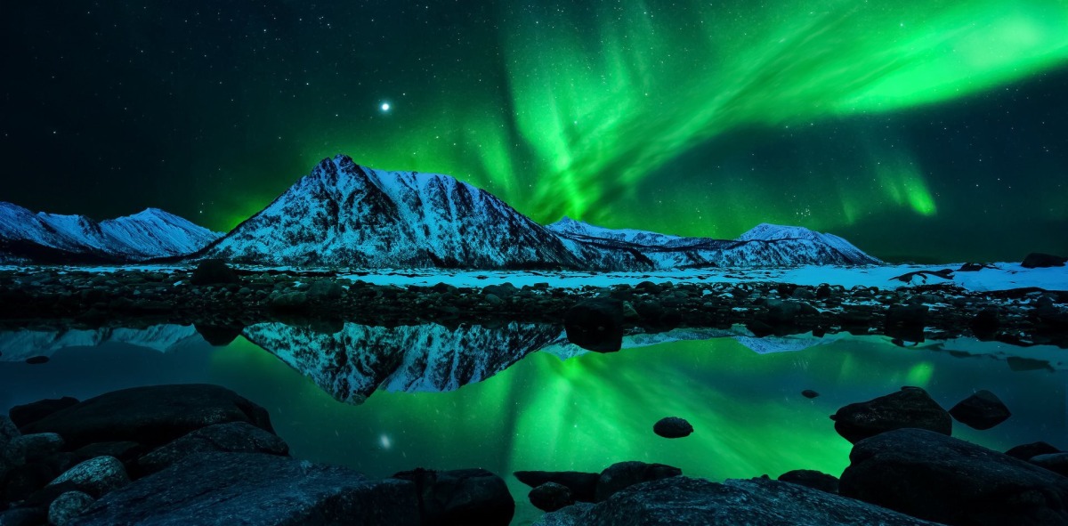 Aurora boreal con un fondo montañoso reflejándose en el mar