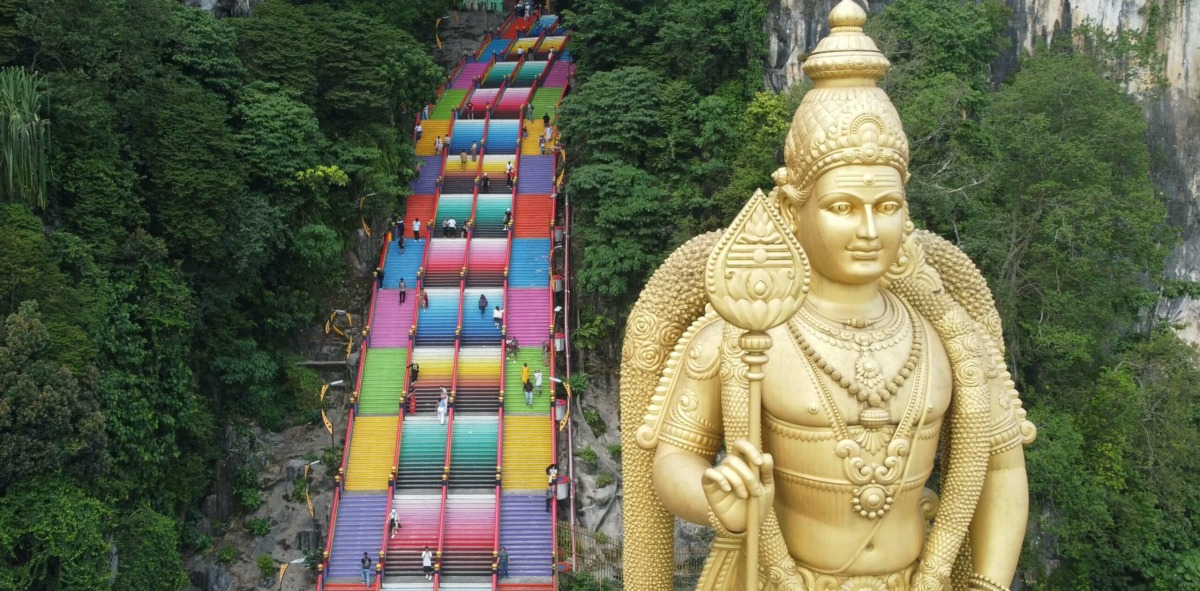 Estatua gigantesca hindú de color oro en una montañas con escaleras de colores a su lado