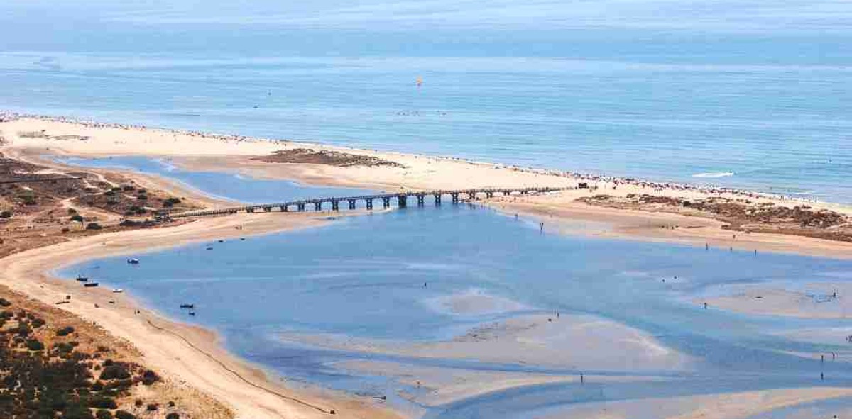 Camino de tierra que va a dar por un puente a una playa