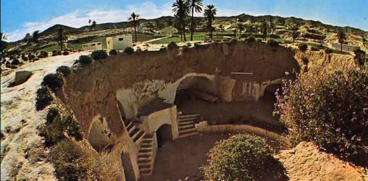 Casas excavadas en el suelo árido, arriba casas con palmeras