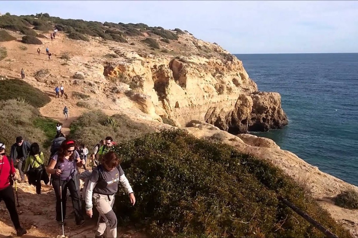 Fila de senderistas por un camino al lado de unos acantilados que dan al mar
