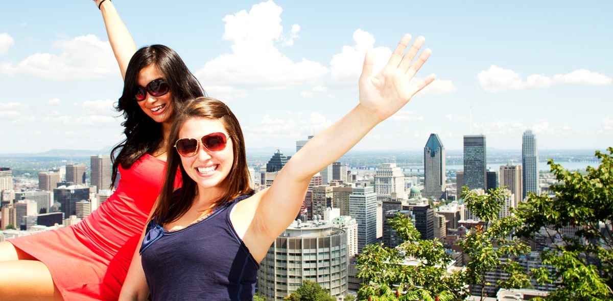dos chicas posando sonrientes con gafas de sol y brazos alzados detrás la ciudad