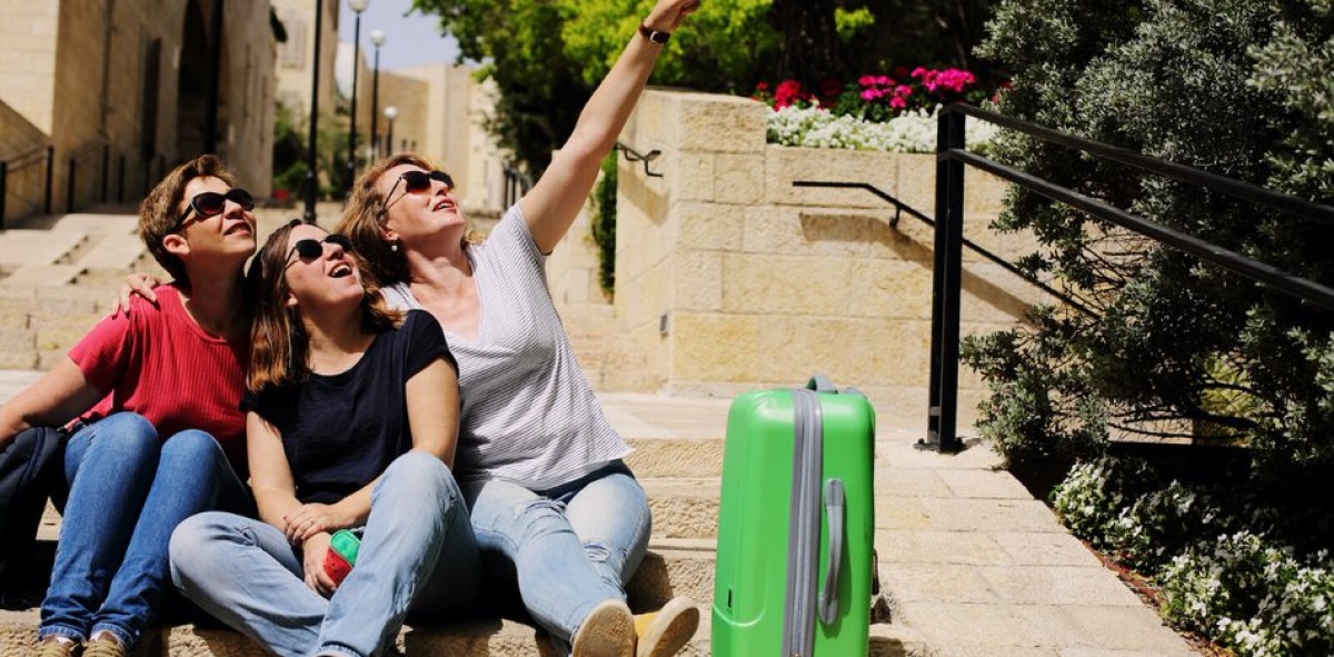 Tras mujeres sentadas en unas escaleras con una maleta haciéndose un selfi