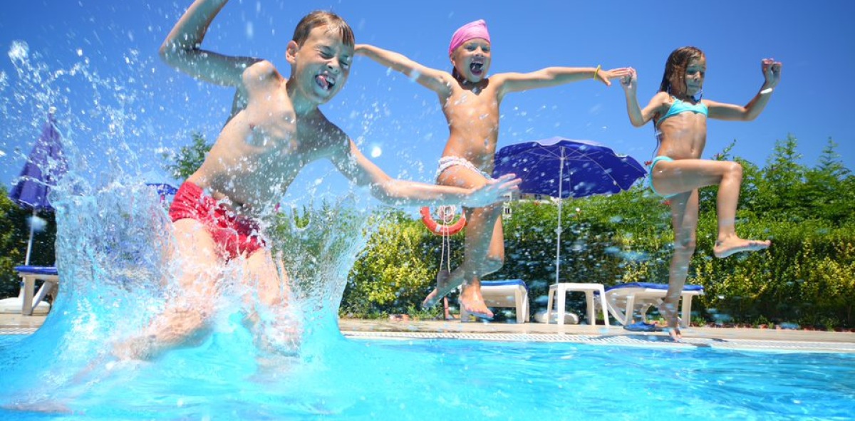 Tres niños en bañador tarándose a la piscina