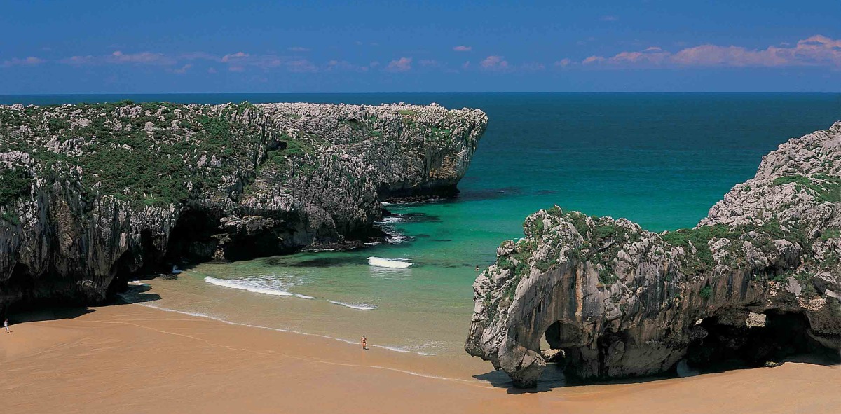 Playa de arena marrón con una entrada de mar entre dos grandes rocas