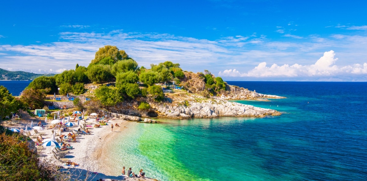 Playa llena de sombrillas en un paisaje de pinos y de aguas cristalinas