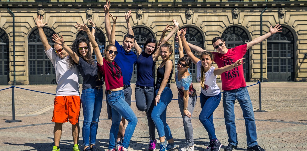 Grupo de Solteros Viajeros posando con los abrazos alzados y al fondo edificio antiguo