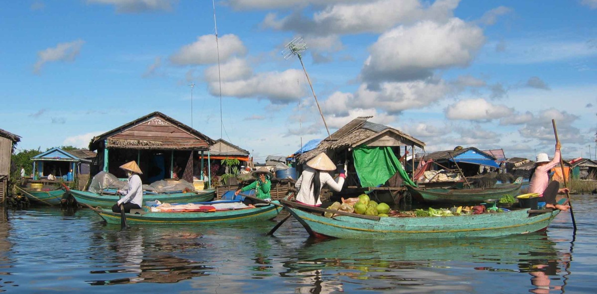 Mujeres en sus canoas vendiendo sus productos, al fondo casas flotantes