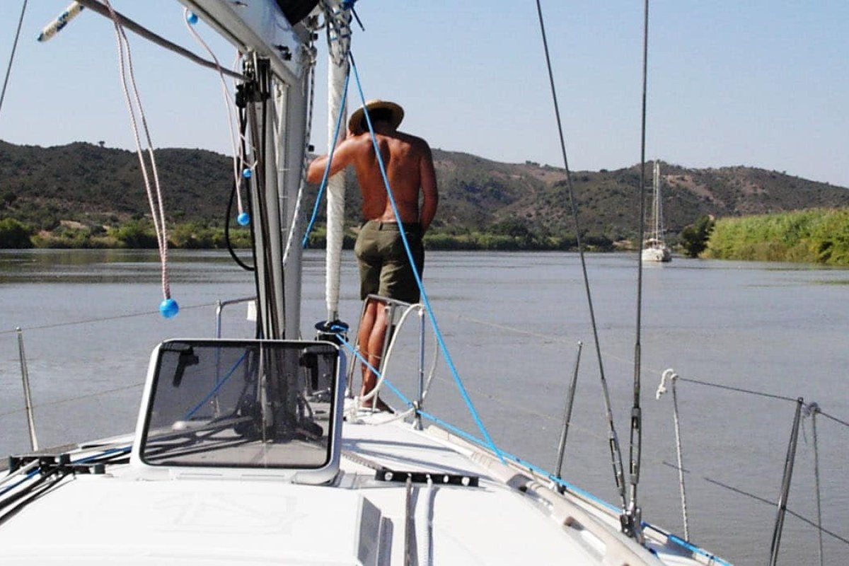 Un hombre de espaldas encima de un velero navegando por un rio