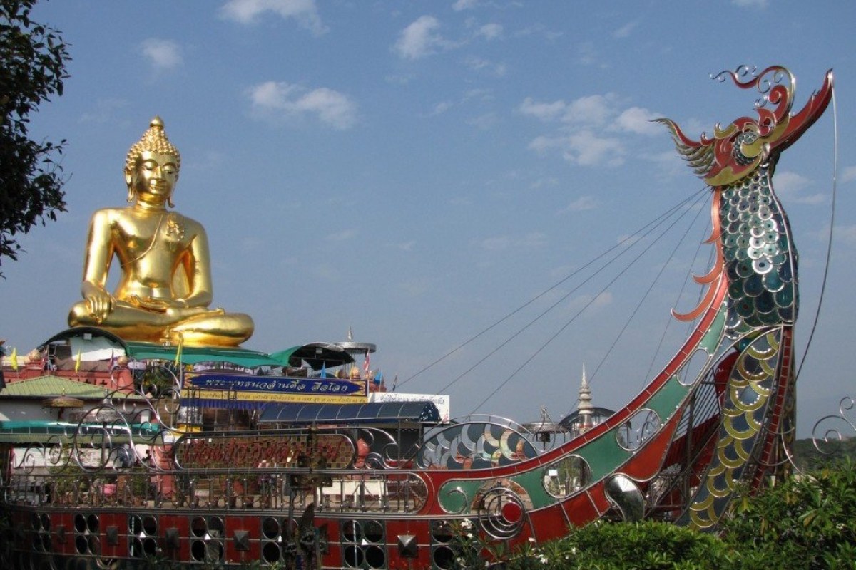Buda sentado de color oro y un barco decorado en vivos colores y la cabeza de un dragón a proa